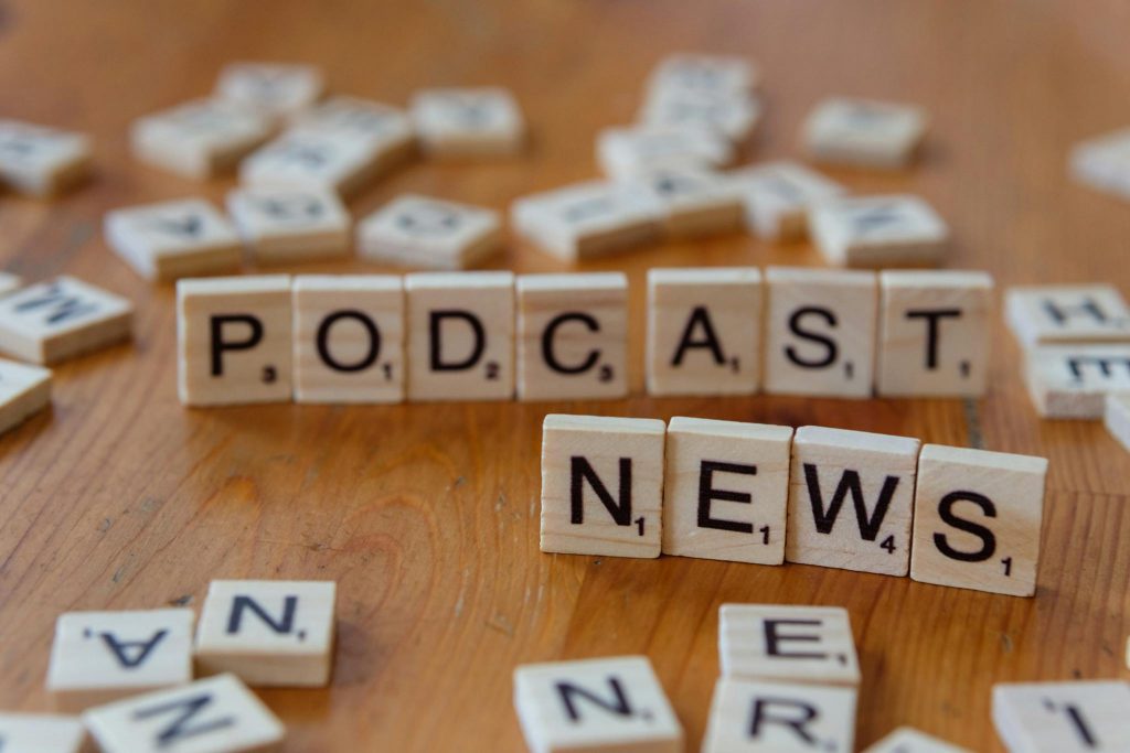 Wooden letter tiles spelling out 'PODCAST NEWS' on a wooden surface.